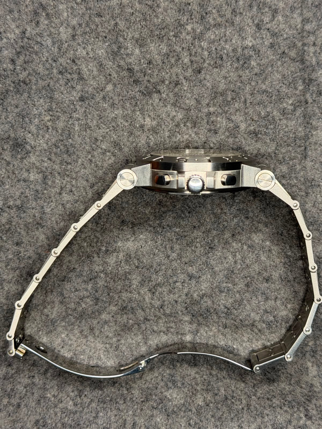 Side profile showing the chronograph pushers, fluted crown and integrated stainless steel bracelet
