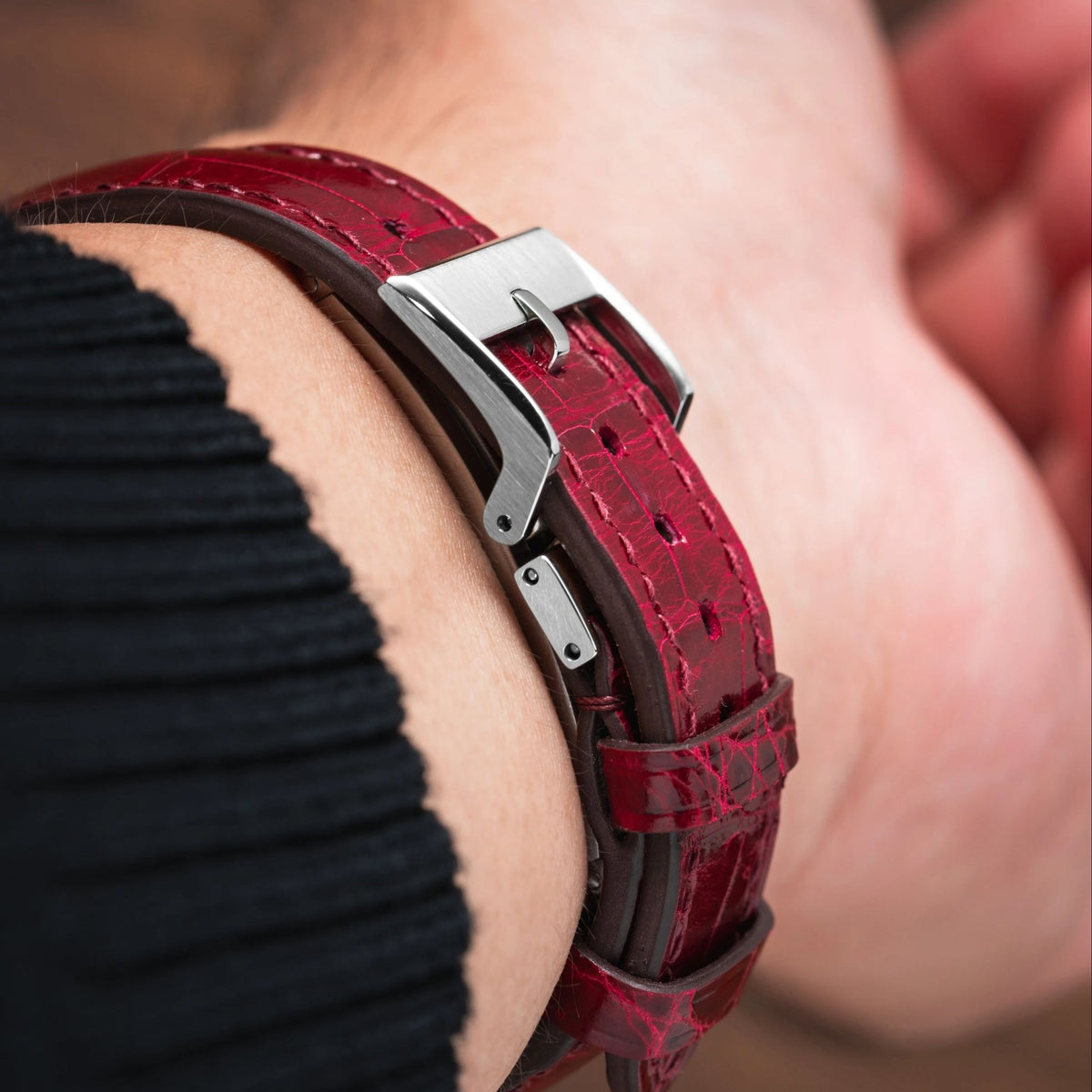 Deployant clasp on a red alligator-grain leather watch strap worn on the wrist