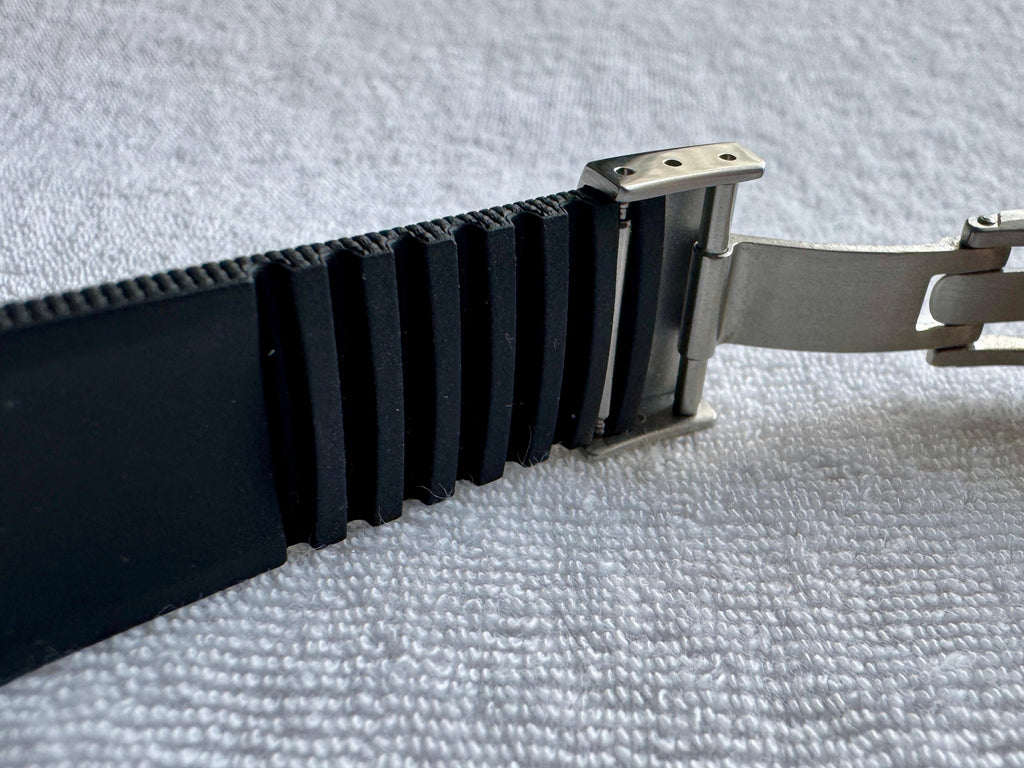 Underside of black rubber watch strap showing ventilated ribbed channels and deployant clasp