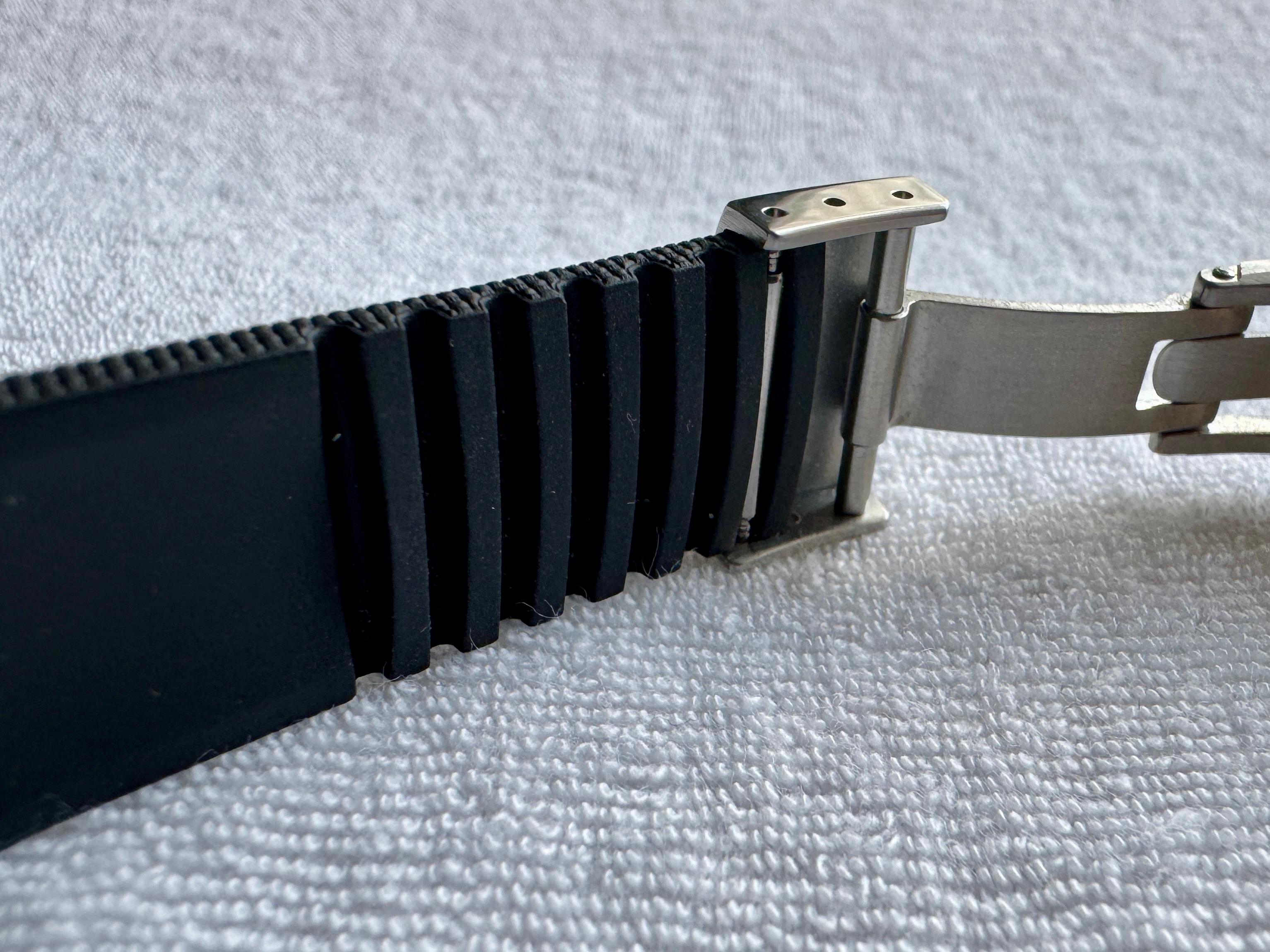 Underside of black rubber watch strap showing ventilated ribbed channels and deployant clasp